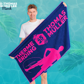 Fussball Star Thomas Müller hält blaues Handtuch mit pinkem Aufdruck "Therme Erding X Thomas Müller". Hintergrund mit Palmenmotiv.